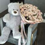 Teddy bear beside a large bouquet of pale pink roses