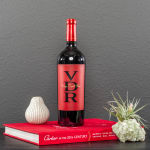 Wine bottle beside a small air plant and decorative vase on a red book