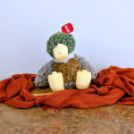 Plush duck toy sitting on a wooden surface with orange fabric draped around it