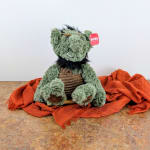 Plush green monster toy with a red tag, sitting on orange fabric