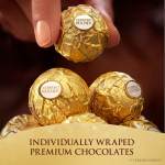 Hand holding Ferrero Rocher chocolates above a box of wrapped chocolates