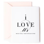 White romantic greeting card with black text reading i love us and a pale pink envelope behind it