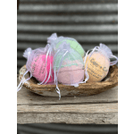Three bath bombs in sheer drawstring bags in a wooden bowl