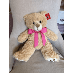 Tan teddy bear with a bright pink ribbon sitting on a chair
