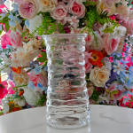Clear ribbed glass vase on a white surface with a floral backdrop