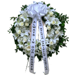 Large white funeral wreath with lilies and roses, topped with a bow and long memorial ribbons.