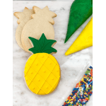 Pineapple-shaped sugar cookies with yellow and green icing bags and rainbow sprinkles on a marble surface