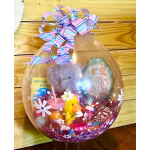 Clear balloon gift with a teddy bear, Easter treats, and a striped ribbon bow