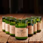 Six green glass candles with kraft paper labels on a wooden surface