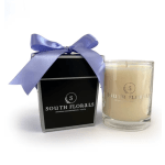 Cream-colored glass candle and black gift box with lavender bow and South Florals logo