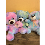 Three pastel tie-dye teddy bears with ribbon bows sit on a wooden surface.