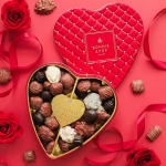Heart-shaped box of assorted chocolates with red roses on a pink background