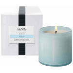 Light blue glass candle burning beside its white box packaging.