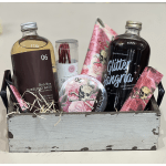 Wooden crate gift set with bath soak, sangria mixer, and pink floral skull-themed self-care items.