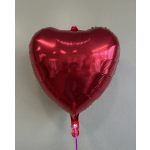 Red heart-shaped foil balloon against a plain wall