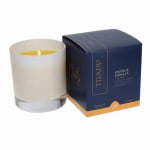 Lit candle in a glass jar beside a navy orange vanilla box