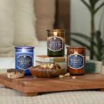 Three scented candles on a wooden tray with a bowl of nuts.