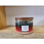 A glass jar candle with a wooden lid and red-green layered wax
