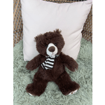 Brown teddy bear with a striped scarf sitting on a chair with a pillow