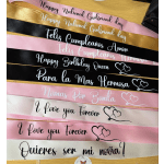 Stacked satin sashes with printed messages in pink, black, white, and gold