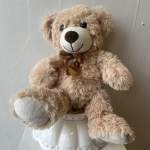 Plush teddy bear with a ribbon sitting on a white ceramic base