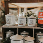 White lidded candles on a wooden shelf beside a coffee bag