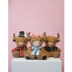 Three plush Highland cow toys with bows and hats on a white pedestal