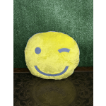 Yellow smiley-face plush pillow on a dark patterned surface