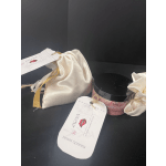 Two satin gift pouches and a pink jar with a black lid on a dark surface