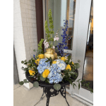 Blue hydrangeas and yellow roses arranged in a gold urn on a black stand
