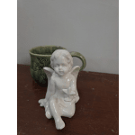 White ceramic angel figurine in front of a green mug