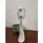 White angel figurine holding a candle, with a green mug behind it