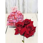 Three red roses beside a pink Valentine gift bag