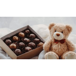 Box of assorted chocolates beside a teddy bear with a red bow