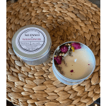 Round tin soy candle with dried pink and yellow wildflowers, shown with its lid on a woven mat