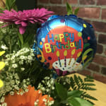 Birthday balloon beside a bouquet of pink, orange, and white flowers