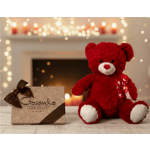 Red teddy bear and decorative chocolate box on a wooden surface with soft candlelight in the background.