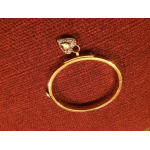 Gold ring with a small diamond-like heart-shaped setting on red fabric