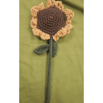 Crocheted sunflower with a long stem on green fabric