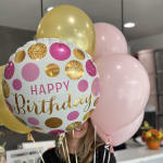 Birthday balloons in pink, gold, and white with a "Happy Birthday" balloon in front