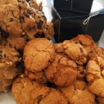 Pile of chocolate chip cookies beside black gift boxes tied with ribbon