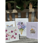 Three greeting cards with floral and birthday designs leaning against a wooden fence