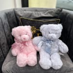 Two plush teddy bears with ribbons sitting on a gray chair