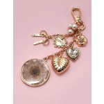 Gold-tone charm keychain with heart and flower pendants on pink background