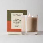 Lit glass candle in front of a Votivo Fresh Tomato Leaf box