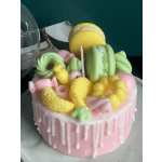 Pink drip cake topped with colorful macarons and candy-like decorations