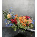 Colorful mixed bouquet in a clear glass vase with blue flowers and roses