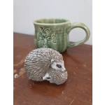 Small hedgehog figurine in front of a green ceramic mug