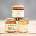 Three jars of wildflower honey stacked on a wooden surface