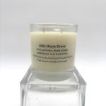 Cream-colored scented candle in a clear glass jar labeled Little Black Dress on a clear stand